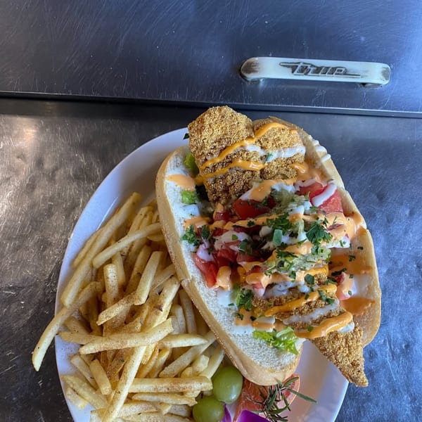 A fried fish po'boy with lettuce, tomato, and sauce, served with french fries and grapes.