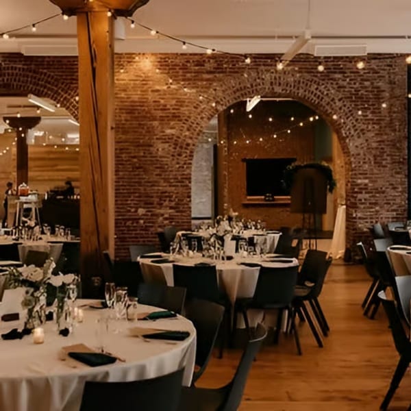 Elegant event space with round tables, white tablecloths, brick arches, and string lights at Po' Shines Cafe.