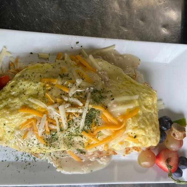 A soul food omelet topped with shredded cheese, herbs, and gravy, served with a fruit skewer.
