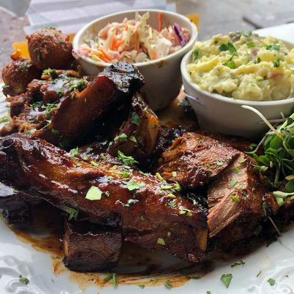 A plate of Po' Shines Cafe De La Soul's BBQ ribs, hush puppies, coleslaw, and mashed potatoes.