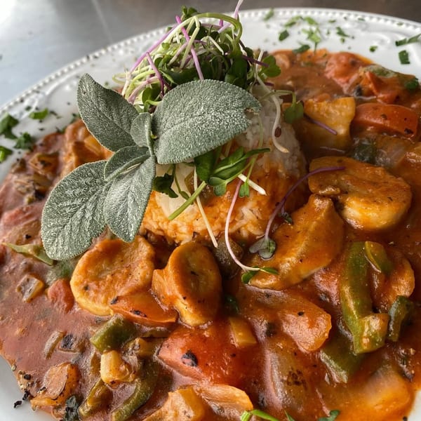 Soul food dish with rice, shrimp, vegetables, and a rich sauce, garnished with herbs.