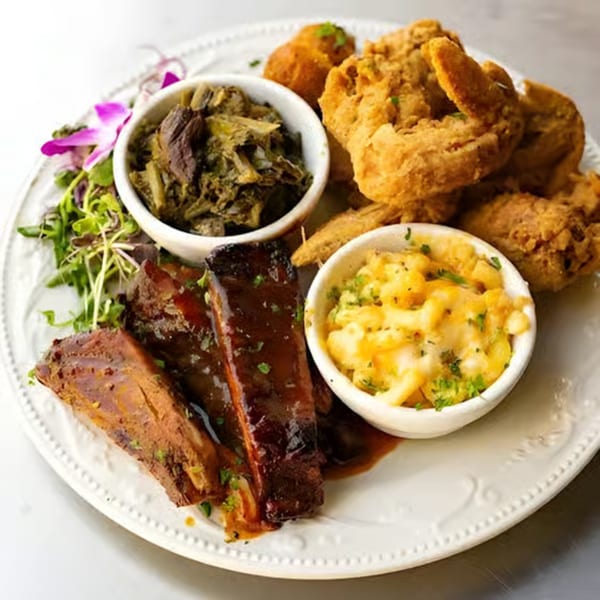 A soul food platter with fried chicken, BBQ ribs, collard greens, and macaroni and cheese.