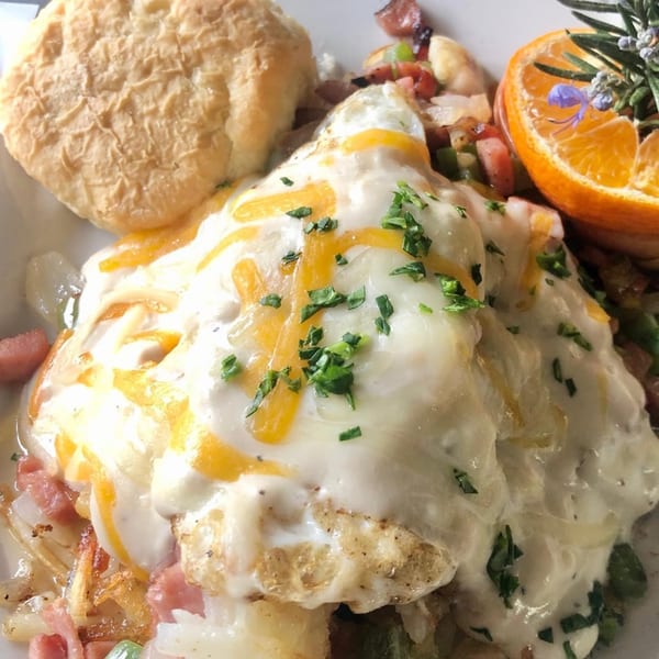 Soul food breakfast with cheesy eggs, biscuit, ham, potatoes, and an orange garnish.