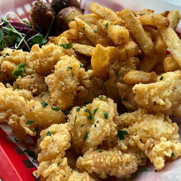 A red basket filled with crispy fried shrimp, golden french fries, and a side of greens.