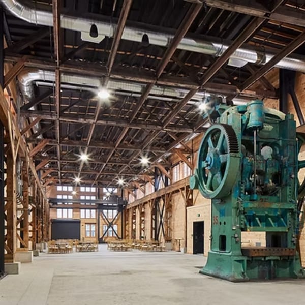 Spacious industrial-style dining hall with high ceilings, exposed wooden beams, and a large green machine.