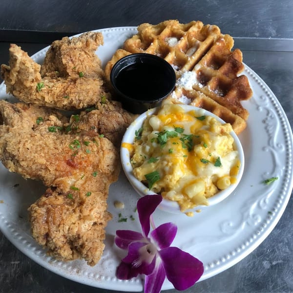 Po' Shines Cafe De La Soul's fried chicken, waffles, mac and cheese, and syrup on a white plate.
